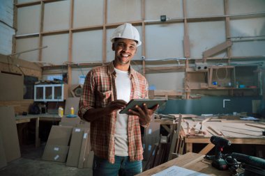 Marangoz ambarında tablet kullanırken gülümseyen Afro-Amerikan. Yüksek kalite fotoğraf