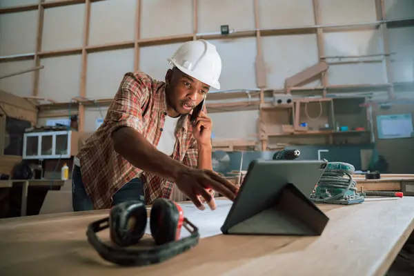 Concentrated African Male Uses Tablet While Phone Woodwork Factory High — Stock Photo, Image