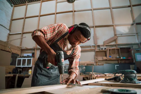 African American carpenter drills a piece of wood in carpentry workshop . High quality photo