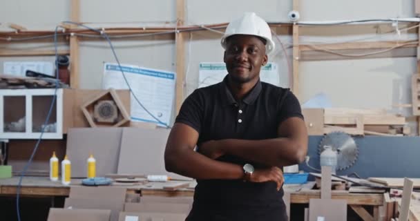カーペントリー工場でビデオのためのハードハットポーズを着用している若いアフリカの男性 高品質の4K映像 — ストック動画