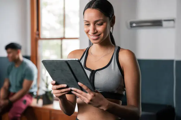 여성은 체육관에서 태블릿 컴퓨터 휴대용 장치를 사용하는 웃고있다 그녀는 이벤트 스톡 사진