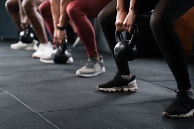 Ayakkabı giyen bir grup insan spor salonundaki dinlenme etkinliğinde eğleniyor. Kalçalarını ve bacaklarını çalıştırmak için su tabancalarıyla çömeliyorlar.