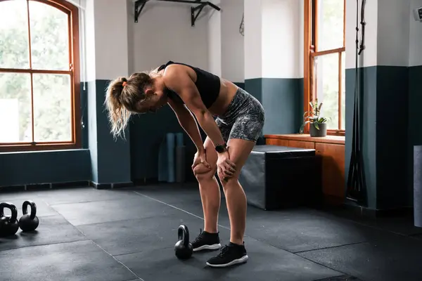 A woman is kneeling on the floor at the gym, working on strengthening her legs and thighs. She is supporting herself with her knees and elbows while also engaging her chest and calves