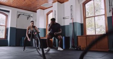 Bir erkek ve bir kadın, ahşap döşemeler ve ahşap döşemelerle çevrili bir spor salonunda iplerle çalışıyor.