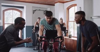 Bir grup insan spor salonunda egzersiz bisikletleri üzerinde çarklar çeviriyor. Etkinliği kaslarını çalıştırırken ve kalçalarını düzeltirken paylaşıyorlar.
