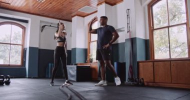 Bir erkek ve bir kadın spor salonunda birlikte spor yapıyor, bacaklarını çalıştırıyor ve etraflarını pencereler, bitkiler ve ahşap döşemeler sarmışken insan bedenlerini güçlendiriyorlar.