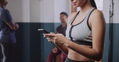 Spor giyinen çok ırklı bir kadın spor salonundaki cep telefonu cihazına gülümsüyor ve gülüyor. Arka planda erkek var. Yüksek kalite 4k görüntü