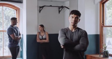 Bir erkek ve bir kadın spor salonundalar, ikisi de kollarını kavuşturmuş, kaslarını gösteriyorlar. Kadın tişört giyiyor ve adamın kafasında şapka var.