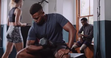 Bir bankta oturan enerjik Afro-Amerikan 'a yaklaş. Ağırlıklarıyla çalışıyor, akıllı saat takıyor. Yüksek kalite 4k görüntü