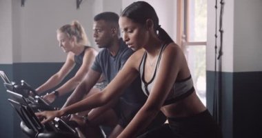 Bir grup birey spor salonunda eğlenceli bir etkinliği paylaşıyor. Egzersiz bisikletleri üzerinde oturup kaslarını kaslarına ve karnına çalıştırıyorlar.
