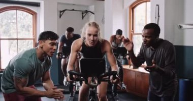 Bir grup insan spor salonunda bisiklet sürmenin eğlenceli etkinliğini paylaşıyor. Pencerenin kenarında oturuyorlar, müziği hissediyorlar ve kaslarını çalıştırıyorlar.