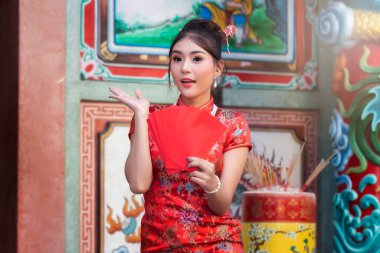 Çin Yeni Yılı 'nı kutlamak için: Kırmızı Cheongsam (qipao) elbiseli Çinli kadın tapınakta kırmızı zarflar (hong bao) taşıyor..