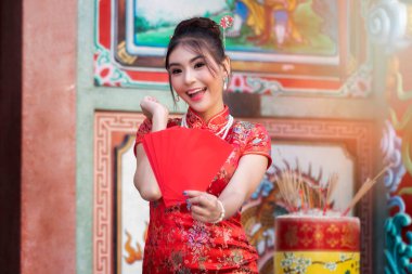 Çin Yeni Yılı 'nı kutlamak için: Kırmızı Cheongsam (qipao) elbiseli Çinli kadın tapınakta kırmızı zarflar (hong bao) taşıyor..