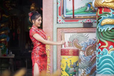 Çin Yeni Yılı 'nı kutlamak için kırmızı Cheongsam elbiseli Çinli kadın elinde tütsü tutarak Çin tanrısına tapınakta hürmetlerini sunar..