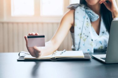 Kredi kartı tutan Asyalı genç bir kadın ve ev ofisteki internet ürünleri için dizüstü bilgisayar kullanıyor. Çevrimiçi alışveriş kavramı.