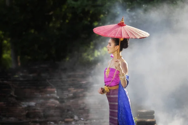 在烟雾弥漫中 美丽的泰国女人穿着红色雨伞的泰国人传统服装 — 图库照片