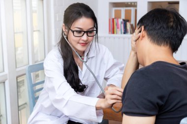 Doktor steteskopla hastayı kontrol ediyor. Hastanedeki ofisinde steteskoplu bir hastanın göğsünü dinleyen bir doktor..