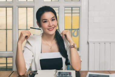 Gülümseyen Asyalı güzel bir kadın elinde kredi kartı ile ödeme yaparken güven ve güven gösteriyor. Çevrimiçi alışveriş kavramı.