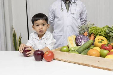 Bir çocuk ve doktor sağlıklı yemek yedikleri için mutlular. Çocuk, taze meyve ve sebze yemeyi seçmek için doktorla beslenme konusunu öğreniyor..