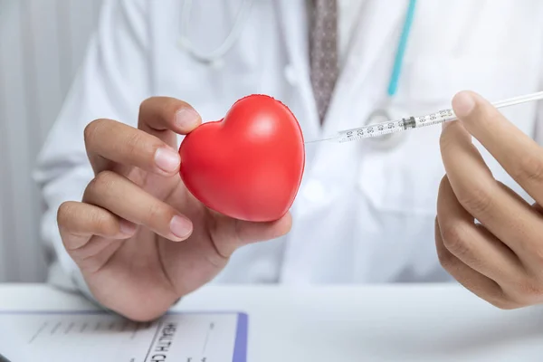 Doctor inject syringe with needle into toy red heart ball. Heart health and cardiology concept.