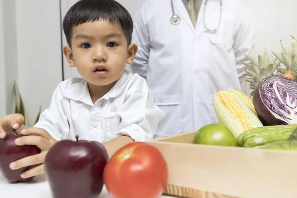 A boy and doctor happy to have healthy food. Kid learning about nutrition with doctor to choose eating fresh fruits and vegetables.