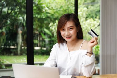 Gülümseyen Asyalı güzel bir kadın elinde kredi kartı ile ödeme yaparken güven ve güven gösteriyor. Çevrimiçi alışveriş kavramı.