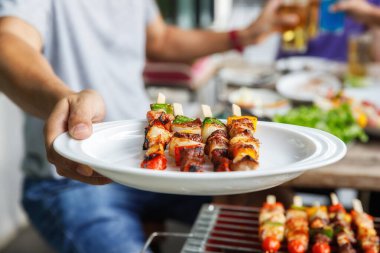 Arkadaşlar arasındaki partide elinde barbekü tabağı olan bir adam. Yiyecek, insan ve aile zaman kavramı.