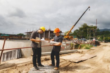 İnşaat işçileri, proje detaylarını inşaat alanındaki planlarla tartışıyor..