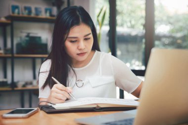 Genç Asyalı kadın, günlük kıyafetlerini giyer ve ofiste çalışır. Sosyal mesafe uygulaması Coronavirus COVID-19 'u engelliyor.