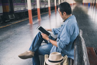 Tren istasyonunda oturan ve akıllı telefon kullanan bir yolcu. Klasik tonda seyahat kavramı.