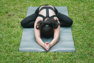 Ateşli çocuk pozisyonunda yoga yapan Asyalı bir kadın ya da açık hava parkındaki mindere oturup eğilen bir çocuk..