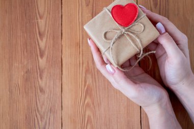 Veren bir hediye kutusu bir jest olarak tutan bir kadın. bir ahşap yüzey zemin üzerinde. Metin için boş alan.