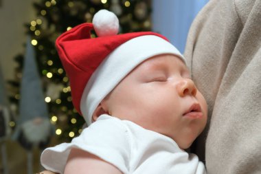 Sevimli bir Noel kıyafetiyle annesinin kollarında huzur içinde uyuyan bir erkek bebek anı. Sahne sıcaklığı, aşkı ve şenlikli ruhu yansıtıyor..