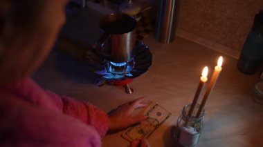 Bir kız mum ışığında gaz ocağını yakıyor ve elektriksiz para sayıyor. Ukrayna 'da Savaş