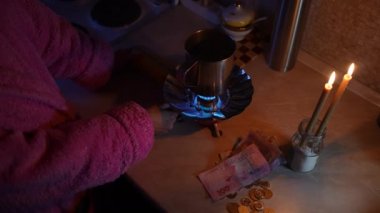 Bir kız mum ışığında gaz ocağını yakıyor ve elektriksiz para sayıyor. Ukrayna 'da Savaş