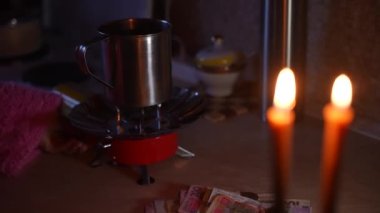 Bir kız mum ışığında gaz ocağını yakıyor ve bardakta su ısıtıyor. Ukrayna 'da savaş. Elektrik ve gaz yok.