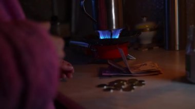Bir kız mum ışığında gaz ocağını yakıyor ve elektriksiz para sayıyor. Ukrayna 'da Savaş