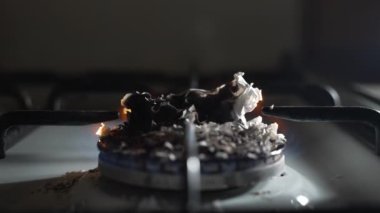 Alacakaranlıktaki bir gaz ocağında yanmış kağıdın külleri. Ağır çekim. Dolly vurdu.
