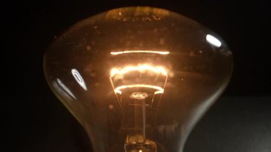Tungsten spiral lamba siyah bir arka planda tel üzerinde sallanıyor. Dolly vurdu. Yakın plan.