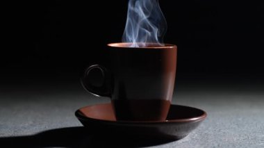 Siyah arka planda, masanın üzerinde sıcak kokulu kahve olan bir fincan. Yavaş çekim
