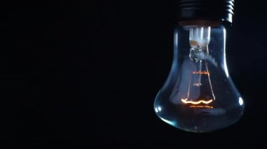 Tungsten spiral parlak lamba siyah arka planda bir tel üzerinde sallanıyor. Dolly vurdu. Yakın plan.