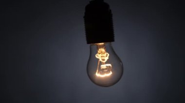 Tungsten spiral lamba siyah bir arka planda tel üzerinde sallanıyor. Yavaş çekim