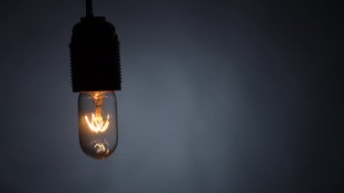 Tungsten spiral parlak lamba, siyah arka plandaki bir kabloda yanıp sönüyor. Dolly vurdu. Yakın plan.