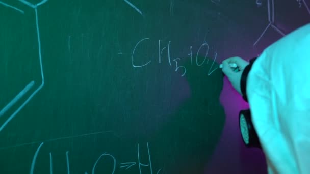 保護スーツの化学者はチョーク付きの黒板に式を書いている スローモーション — ストック動画