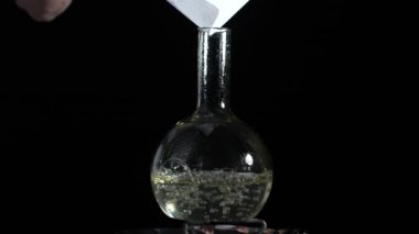 Kaynama çözeltisi olan cam bir laboratuvar şişesine beyaz bir toz dökülüyor. Laboratuvarda uyuşturucu al. Yavaş çekim