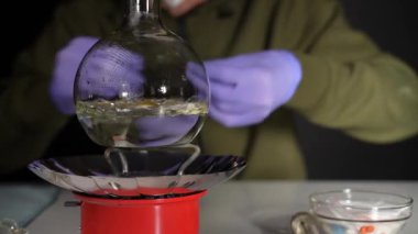 Yeraltı laboratuarındaki bir kimyager gaz ocağında cam bir şişede ilaç pişiriyor.