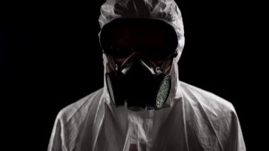 Kimyasal koruma giysisi giymiş bir laboratuvar çalışanı siyah arka planda pantolonunu indiriyor.
