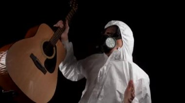 Kimyasal korumalı bir adam siyah arka planda gitarla dans ediyor.