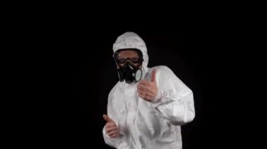Kimyasal koruma giysisiyle dans eden bir adam solunum cihazı ve siyah bir arka planda gözlük takıyor.