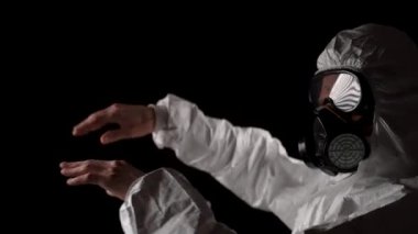 Kimyasal koruma giysisiyle dans eden bir adam solunum cihazı ve siyah bir arka planda gözlük takıyor.